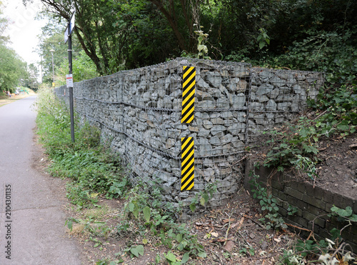 Stone wall retained by steel mesh with warning stripes