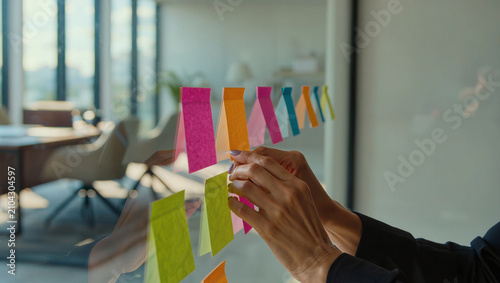 Hands Arranging Colorful Sticky Notes on Glass Office Board