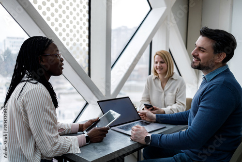Discussion among three people in a modern office setting with large windows