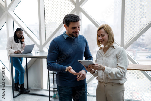 Two people discuss information while standing in a modern office space