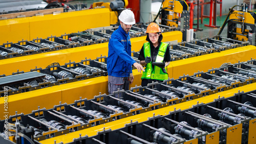 professional engineer,worker,technician use clipboard discuss work, walk in steel metal manufacture factory plant industry. Black African American man and woman wear hard hat check quality machine.