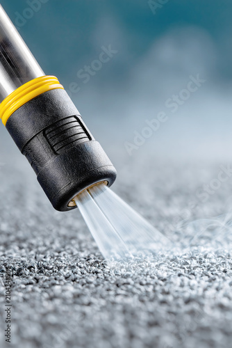 Water is sprayed from a nozzle onto a gray surface in a controlled setting during daytime