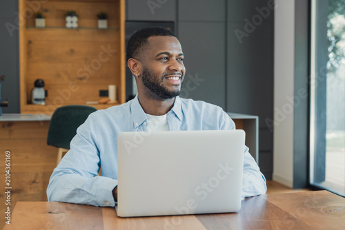 Tableau sur toile Smiling black man using a laptop and looking away, showcasing remote work flexib