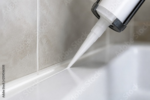 White caulk being extruded into bathroom tile gaps.
