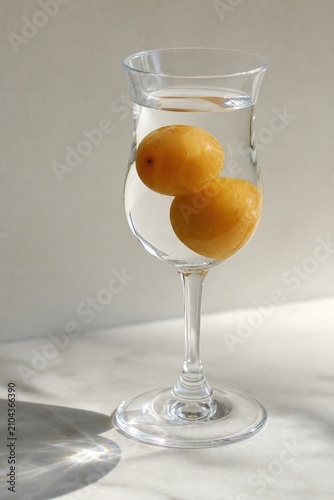 Crystal glass filled with clear plum schnapps and whole fruits, natural light.
