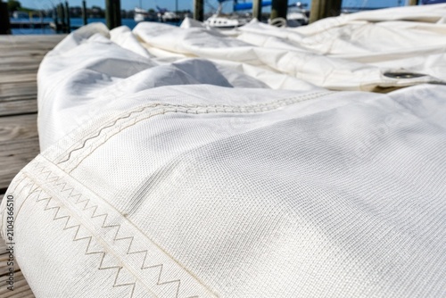 A large expanse of heavy white sailcloth laid out on a dock in bright sun.