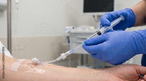 A nurse in blue gloves carefully administers medication through an IV line inserted into a patient's arm in a medical setting.
