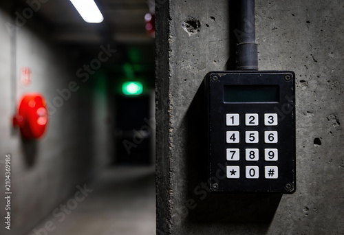 Black security access control keypad on a concrete wall in a dimly lit industrial hallway