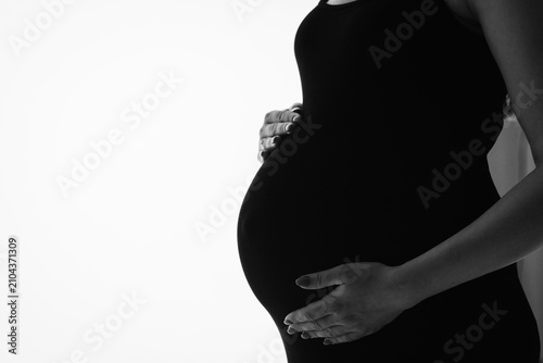 Silhouette of a pregnant woman holding her belly, black and white artistic photo on a white background with empty copy space for text. Concept of motherhood, anticipation, and advertising.