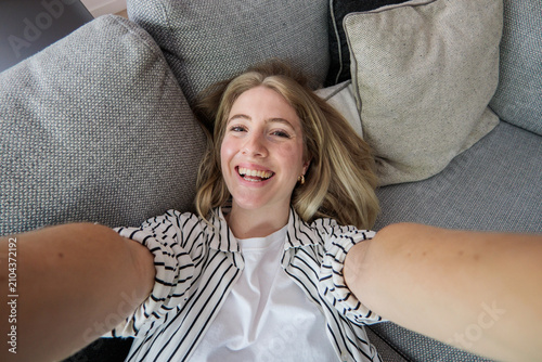 Fotografie Young woman smiling happily directly at the camera, capturing a selfie from abov