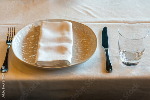 Restaurant place setting with ceramic plate folded napkin drinking glass and cutlery prepared for guest dining experience