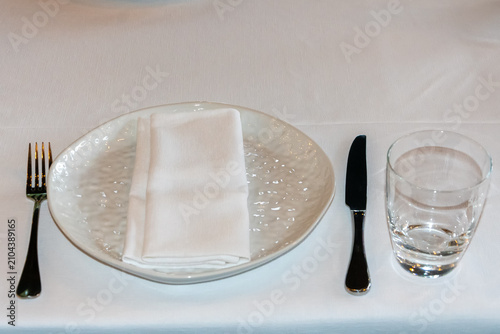 Elegant restaurant place setting with ceramic plate folded napkin cutlery and drinking glass prepared for hospitality service