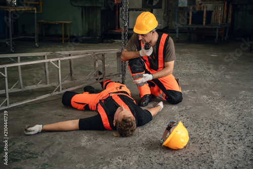 Factory Emergency with a Worker Using a Radio While Kneeling Beside an Unconscious Colleague After a Workplace Accident on the Production Floor