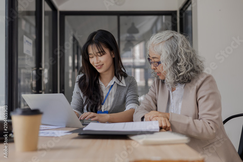 Foto Two Asian businesswomen from different generations working happily together on l