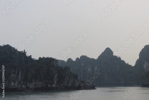 Rocky limestone karst formations towering over calm emerald waters in ha long bay.