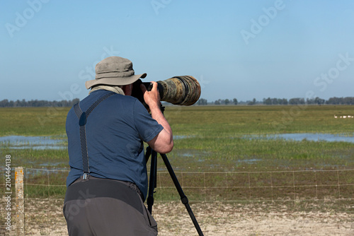 Hombre mayor fotografiando aves con trípode.