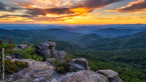 Breathtaking vibrant sunset paints the dramatic mountain landscape with lush green forests and ancient rock formations