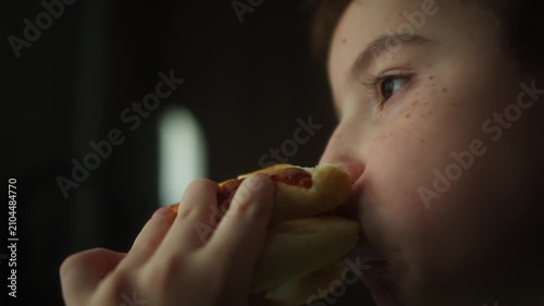 Close up of a child taking a bite of a homemade burger with fresh lettuce and a soft bun. Natural eating moment highlighting a tasty homemade meal and healthy appetite.
