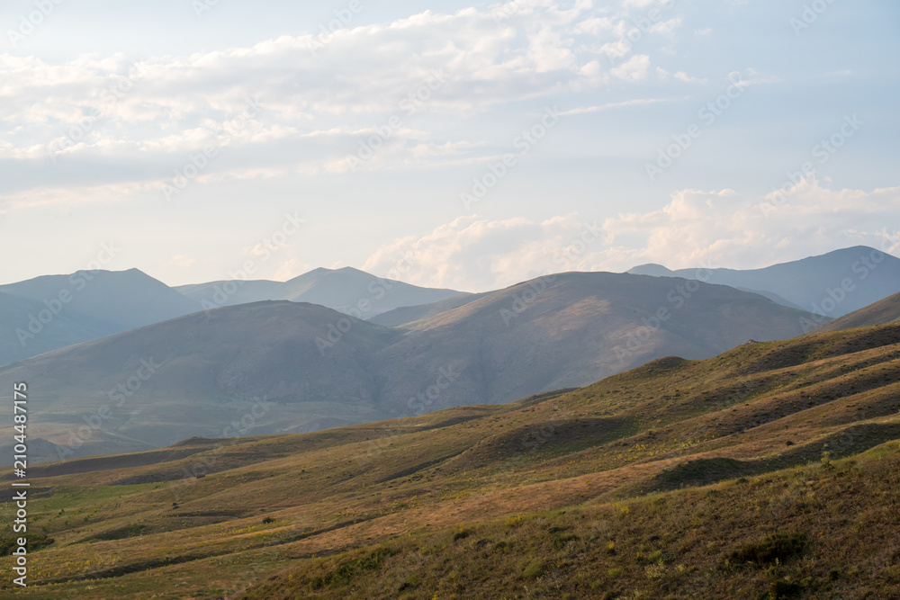 Obraz premium Vast open hills fade into layered mountain ridges under a partly cloudy sky