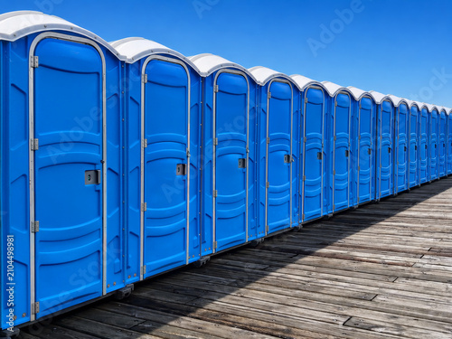 Modern blue portable toilets lined up on a wooden pier. Outdoor toilet cabins for events. Detail of mobile plastic public restrooms. Public hygiene and street furniture.
