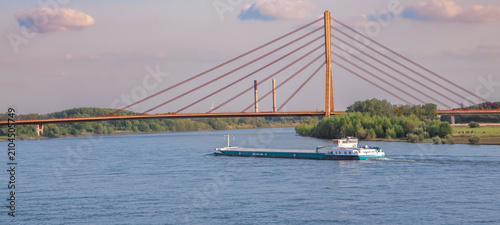 A cargo vessel navigates the Rhine River beneath a cable-stayed bridge in Wesel, Germany, showing inland shipping, infrastructure and European logistics.