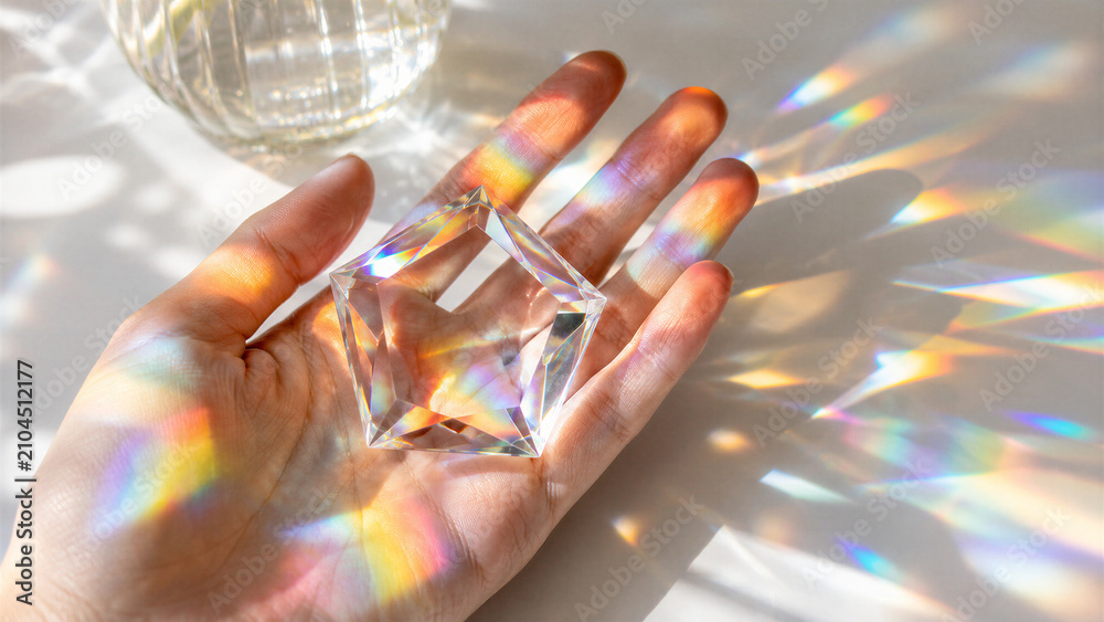 Obraz premium Hand holding glass prism casting rainbow light on surface