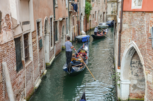 Italy, Venice, Octoberber 01, 2025, A gondolier in a black and white striped shirt is transporting tourists in Venice