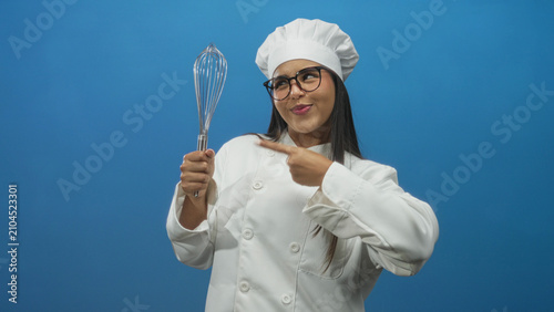 Foto Chef woman points finger to stainless steel whisk and holds its handle in studio while smiling and wearing glasses; joy confidence celebration