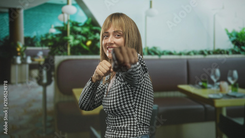 Foto Woman with clenched fists raised in a playful boxing gesture at a restaurant booth inside a building; confidence