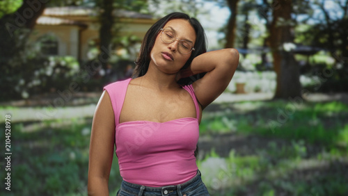 Canvas Print Woman touching neck with hand on neck for neckache, bare shoulder and pink tanktop visible in building courtyard; discomfort reflection