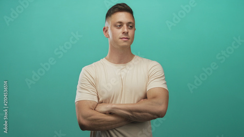 Foto Man with arms crossed revealing muscular biceps and forearms, neutral gaze against teal studio backdrop; confidence strength