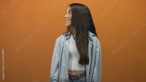 Foto Woman points finger to the right and then gives thumbs up, bare hand and exposed midriff visible against orange backdrop studio; joyful confidence