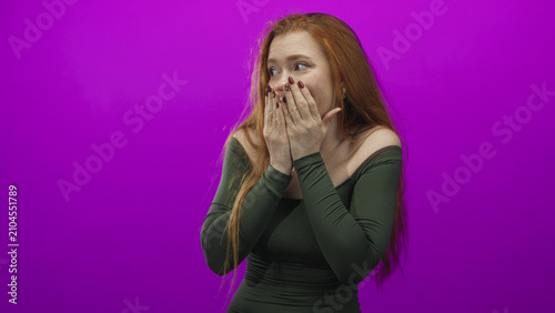 Konstfotografi Woman covers mouth with hands, smiling with bare shoulders against vivid purple studio backdrop while glancing sideways; surprise playful reaction