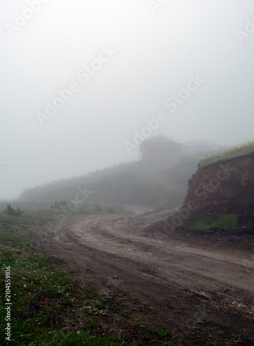 Cuadro en lienzo Winding muddy dirt road leading to a lonely house on a hill shrouded in dense mo