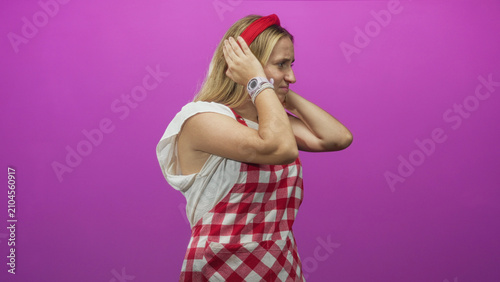 Canvastavla Woman chef in red check apron covers ears with hands, wincing and looking pained against magenta studio wall; stress anxiety
