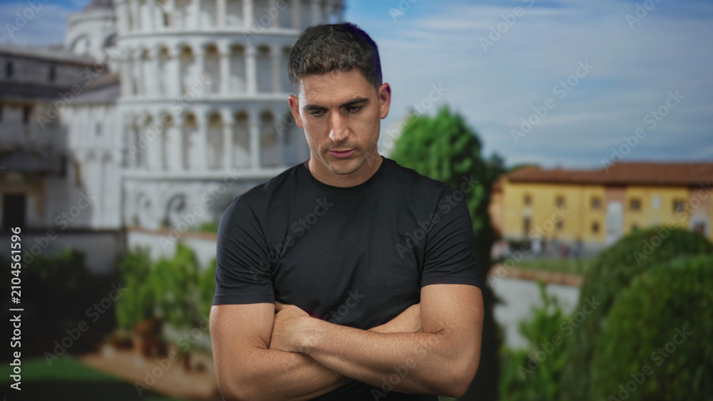 Fototapeta premium Man with arms crossed and head down by a building at the pisa tower outdoor plaza, contemplating the scene; pensiveness reflection.