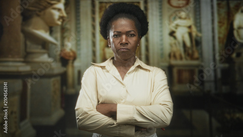 Konstfotografi Woman with crossed arms and stern face in front of marble statues and columns inside a historic building; disapproval resolve