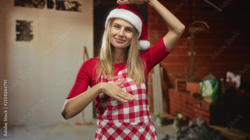 Obraz premium Woman in santa hat and checkered apron, hand placed over chest in a brick building kitchen scene; holiday joy.