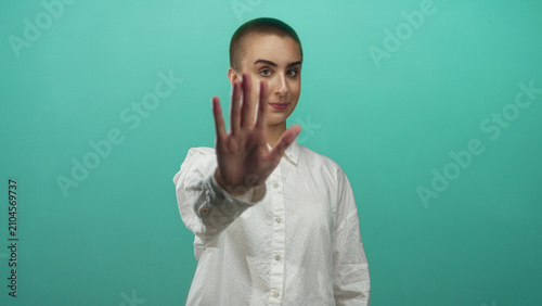 Bild auf Leinwand Woman with short hair holds hand palm outward in stop gesture while wearing white shirt in studio, facing camera; defiance boundary