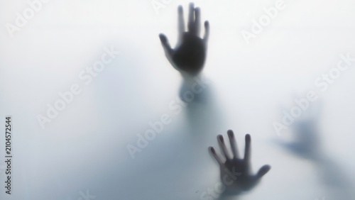 Dark hand silhouettes pressed against frosted glass