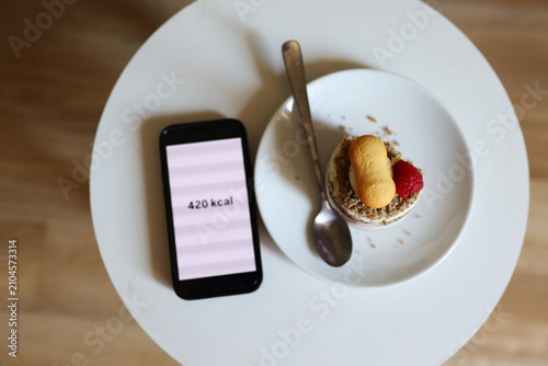 Flat lay of cake and mobile calorie tracker app, highlighting nutrition awareness, portion control and balanced food choices.