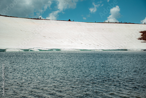 Glacial Mountain Lake Shoreline Showing Melting Glacier Ice, Red Volcanic Soil, and Deep Blue Water