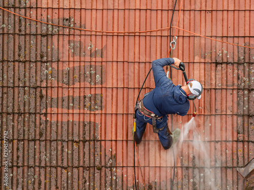 Roof cleaning with pressure washer on historic building during renovation and maintenance of traditional roof tiles. Professional roof cleaning service using pressure washer