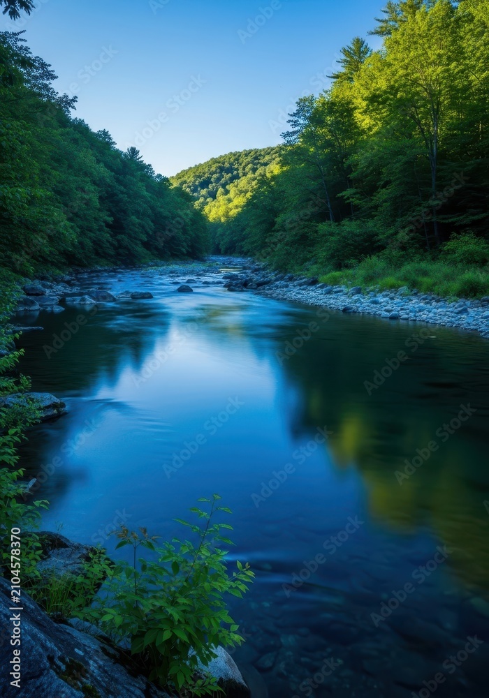 Obraz premium A serene blue river flows gently through a lush green valley during a bright afternoon, reflecting the clear sky and surrounding nature, daytime, ripple, movement