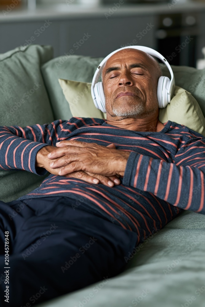 Fototapeta premium Older man lying on sofa with headphones for relaxation background and meditation banner design