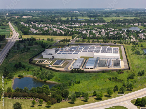 Aerial view of a data center with solar panels on the roof, AI center structure surrounded by roads and green countryside areas	