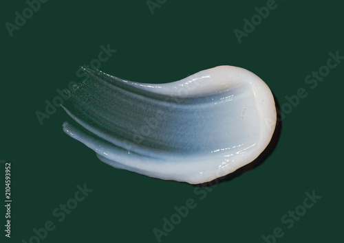 A smooth stroke of white cosmetic cream texture isolated on dark green background, soft gel or lotion swatch closeup