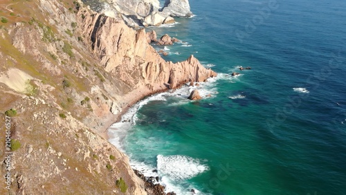 Fotografía Aerial view of rugged coastal cliffs beside turquoise ocean waves and rocky shoreline in bright daylight