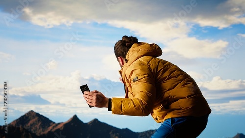 Tableau sur toile A careless traveler drops his smartphone from a cliff and loses balance on a steep mountain peak, placing himself in immediate danger through reckless behavior in the wilderness