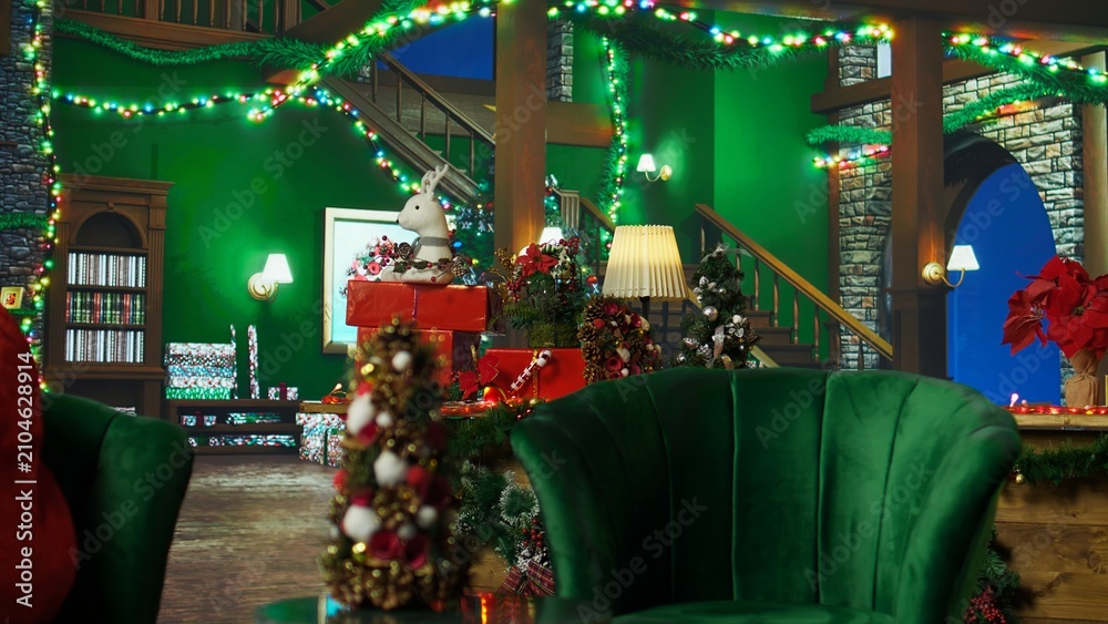 Fototapeta premium A reindeer toy sits in an empty Christmas room decorated with a tree, lights and stockings, adding a playful plush animal detail to the festive Santa Claus workshop setting during the holiday season.